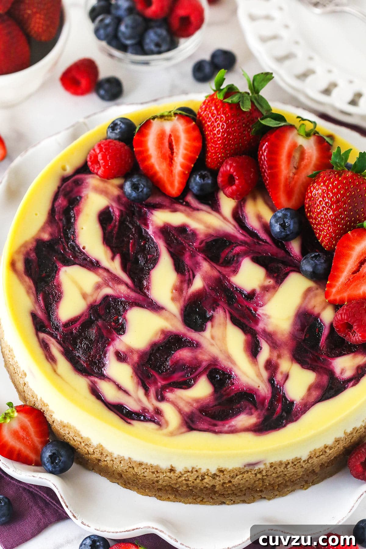 Triple Berry Cheesecake Recipe with Fresh Mixed Berries 17 triple berry cheesecake on white ruffle platter with fruit around it