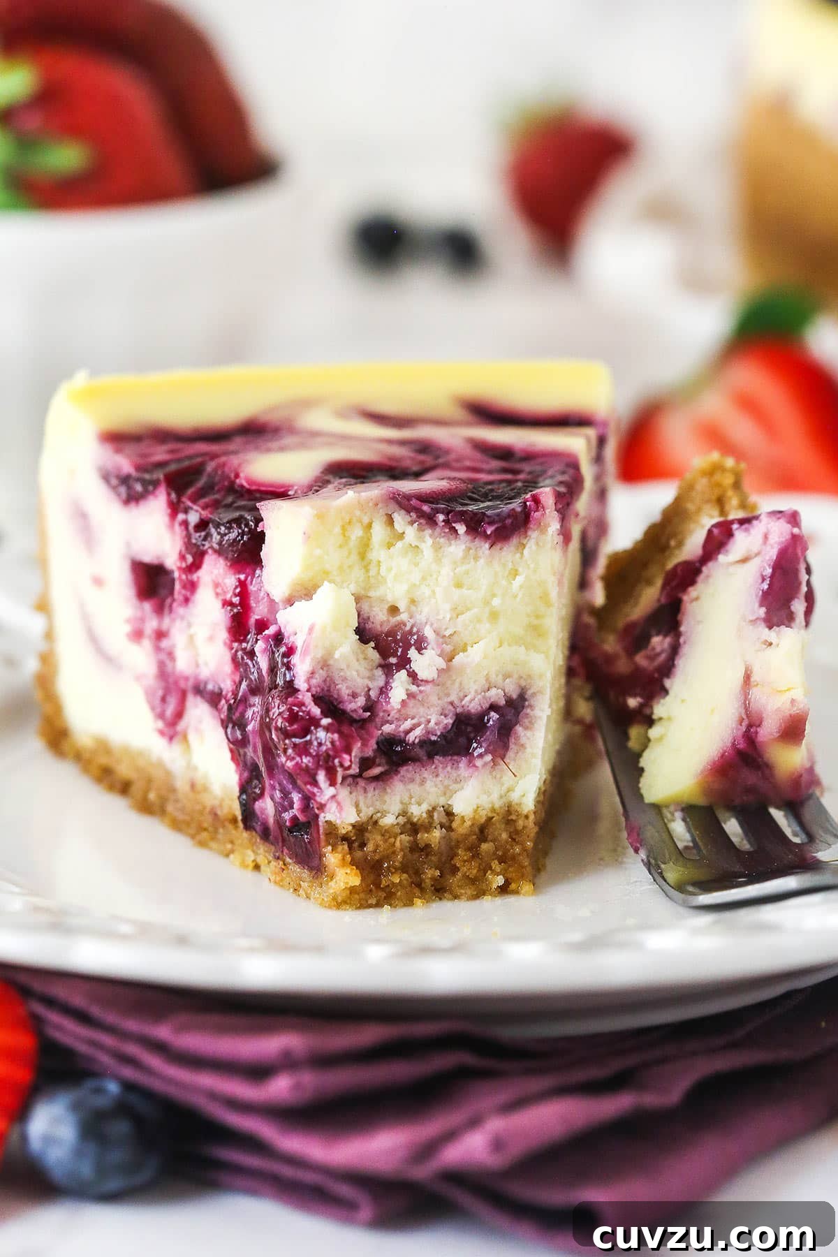 Triple Berry Cheesecake Recipe with Fresh Mixed Berries 18 slice of triple berry cheesecake on white plate with a bite taken out