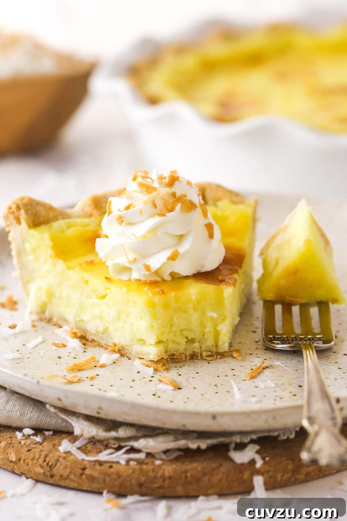 With a thick, creamy custard in a flaky, buttery pie crust, this coconut custard pie delivers just the right amount of coconut flavor. A slice of coconut custard pie on a white plate with a bite on the fork next to it.